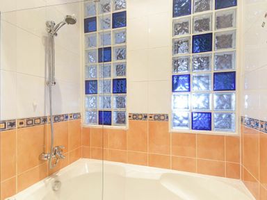 A bathtub with a showerhead and two glass block windows in a bathroom with white and orange tiles at Farne Lookout in Seahouses