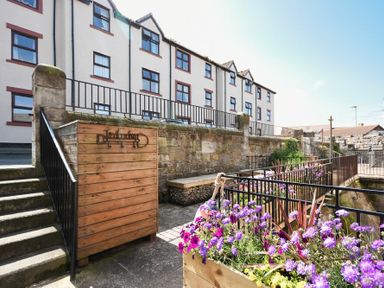 An outdoor area with stairs, a wooden sign, railing, and flower boxes in front of a multi-story building at Farne Lookout in Seahouses