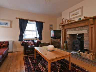 A living room with leather armchairs wooden coffee table fireplace and television at Turnstone Cottage Nr Bamburgh