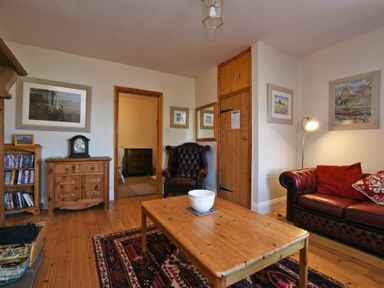 A living room with a wooden coffee table a black leather armchair a red leather sofa with cushions wooden floor and framed pictures at Turnstone Cottage Nr Bamburgh
