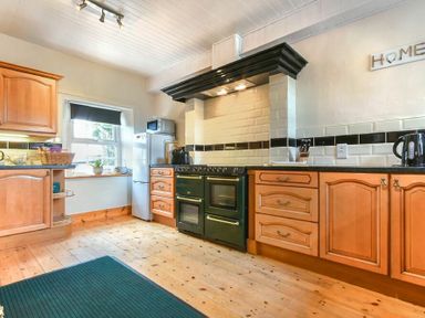 A kitchen with wooden cabinets and black countertop a green stove a refrigerator and a window with a roller blind at Turnstone Cottage Nr Bamburgh