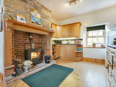 A kitchen with wooden cabinets a wood burning stove and a window at Turnstone Cottage Nr Bamburgh
