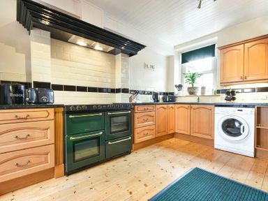 A kitchen with wooden cabinets a green oven a washing machine and a window at Turnstone Cottage Nr Bamburgh