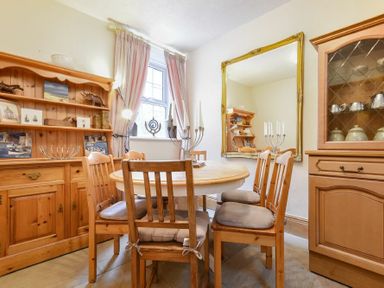 A dining room with a round wooden table and six wooden chairs near a window with pink curtains at Turnstone Cottage Nr Bamburgh