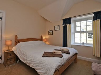 A bedroom with a wooden double bed bedside tables lamps and a window with curtains at Turnstone Cottage Nr Bamburgh