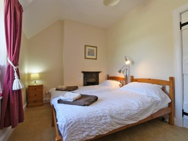 A bedroom with two single beds a bedside table with a lamp and pink curtains at Turnstone Cottage Nr Bamburgh