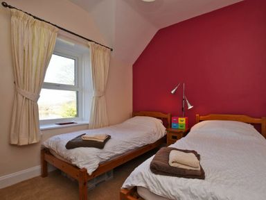 A bedroom with two single beds a window with curtains and a red accent wall at Turnstone Cottage Nr Bamburgh
