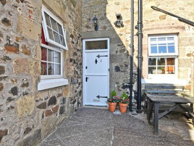 A stone-walled entrance with a white door numbered 2 two potted plants and a wooden bench and table at Turnstone Cottage Nr Bamburgh