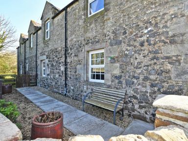 A stone wall cottage with windows a bench and a paved path with plant pots at Turnstone Cottage Nr Bamburgh