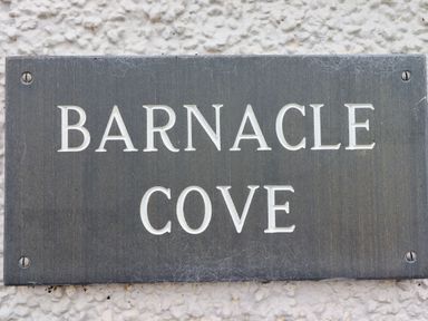 A grey rectangular plaque with the text Barnacle Cove mounted on a white textured wall