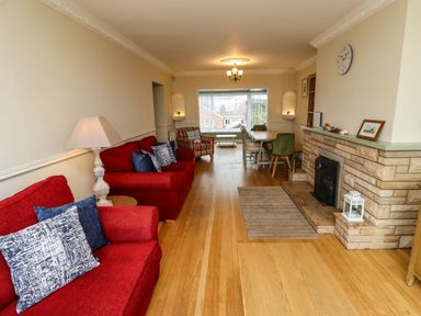 A living room with red sofas a fireplace and a dining table at Barnacle Cove in Beadnell