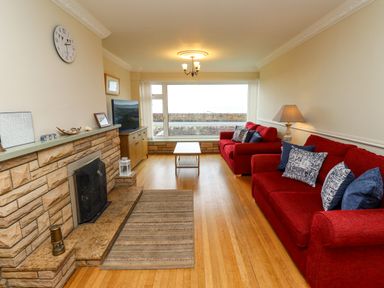 A living room with red sofas wooden floor and large window at Barnacle Cove in Beadnell