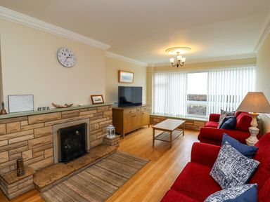 A living room with red sofas a wooden coffee table a fireplace and a television at Barnacle Cove in Beadnell