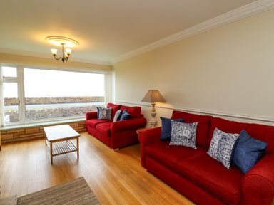 A living room with two red sofas a wooden coffee table and a lamp by the wall at Barnacle Cove in Beadnell