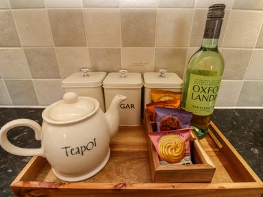 A kitchen tray with a teapot three storage canisters biscuits and a bottle of wine on a countertop at Barnacle Cove in Beadnell