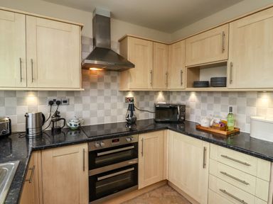 A kitchen with light wood cabinets black countertops a double oven microwave toaster kettle and utensils at Barnacle Cove Beadnell