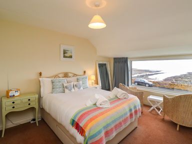 A bedroom with a bed bedside table chairs and a window overlooking a rocky shoreline at Barnacle Cove in Beadnell