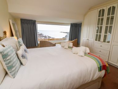 A bedroom with a bed facing a large window overlooking the sea at Barnacle Cove in Beadnell