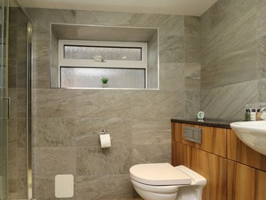 A bathroom with a toilet paper holder window and wooden cabinet at Barnacle Cove in Beadnell