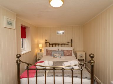 A bedroom with a metal bed frame bedside tables with lamps and a window with a red blind at Barnacle Cove in Beadnell