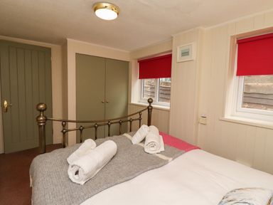 A bedroom with a metal bed frame rolled white towels on a gray blanket green double doors and two windows with red blinds at Barnacle Cove in Beadnell