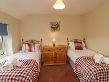 A bedroom with two single beds a wooden cabinet and a lamp at Barnacle Cove in Beadnell