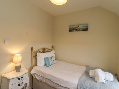 A bedroom with a single bed bedside table with lamp and towels on the bed at Barnacle Cove Beadnell