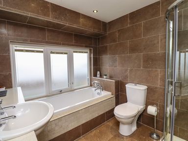 A bathroom with a bathtub next to a window a toilet a sink and a glass shower enclosure at Barnacle Cove in Beadnell