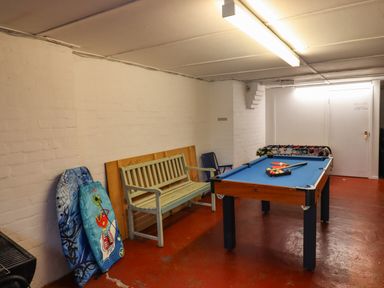 A game room with a pool table a wooden bench and two bodyboards leaning against a white brick wall at Barnacle Cove in Beadnell