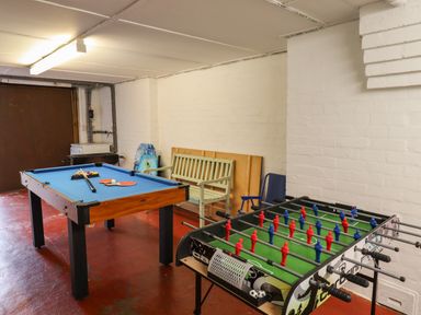 A game room with a pool table and a foosball table with a bench against the wall at Barnacle Cove in Beadnell