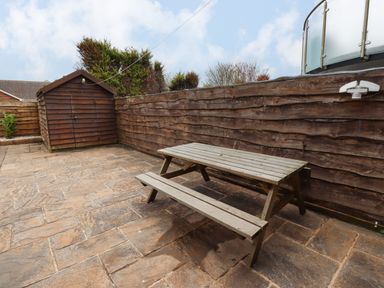 An outdoor patio with a wooden picnic table and a wooden shed against a wooden fence at Barnacle Cove in Beadnell