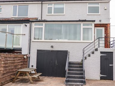 Backyard area with picnic table stairs leading to white door and double black garage doors at Barnacle Cove in Beadnell