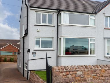 Exterior view of a semi detached house with stone wall and driveway at Barnacle Cove in Beadnell