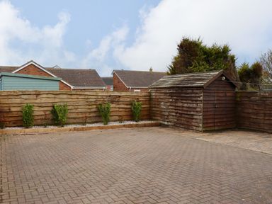 A paved yard with a wooden shed and a wooden fence with small plants along it at Barnacle Cove in Beadnell