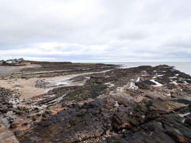 Rocky shore with patches of sand and pools of water by the sea under a cloudy sky at Barnacle Cove in Beadnell