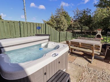 A hot tub with an outdoor table and wooden bench at Rosefinch in Lucker