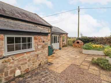 A stone exterior of a cottage with a paved patio garden and outdoor brick oven at Adderstone Cottage in Bamburgh