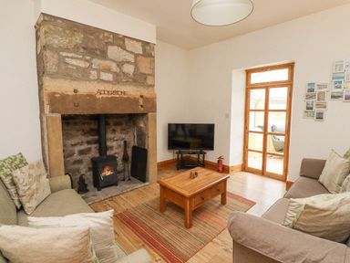 A living room with a stone fireplace wooden coffee table two sofas and a television at Adderstone Cottage in Bamburgh