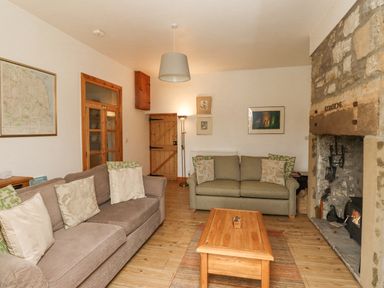 A sitting room with two sofas a wooden coffee table a stone fireplace and a wooden door at Adderstone Cottage in Bamburgh