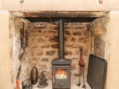 A stone fireplace with a wood burning stove and metal fireplace tools at Adderstone Cottage in Bamburgh