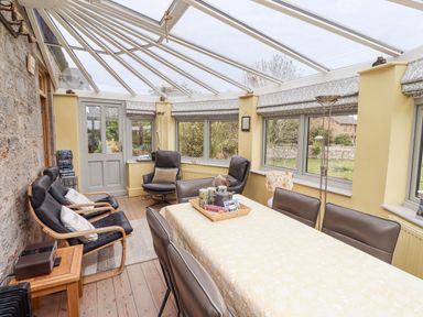 A conservatory with a dining table and chairs and armchairs near windows at Adderstone Cottage Bamburgh