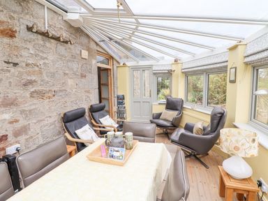 A conservatory with leather chairs a table with cups and a teapot and windows showing a garden at Adderstone Cottage in Bamburgh
