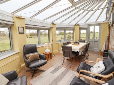 A conservatory with chairs a dining table and windows showing a field at Adderstone Cottage in Bamburgh