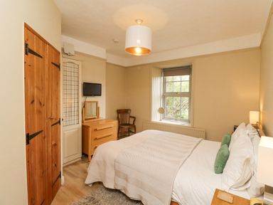 A bedroom with a bed a wooden dresser a chair and a window at Adderstone Cottage Bamburgh