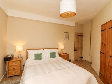 A bedroom with a double bed wooden bedside tables lamps wooden door and wardrobe at Adderstone Cottage in Bamburgh