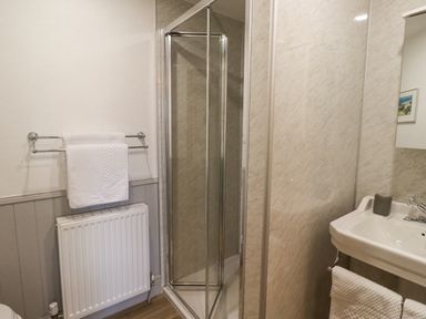 A bathroom with a shower enclosure a radiator with a towel a sink and a mirror at Adderstone Cottage Bamburgh