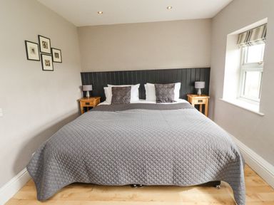 A bedroom with a double bed two bedside tables lamps and framed pictures on the wall at Adderstone Cottage in Bamburgh