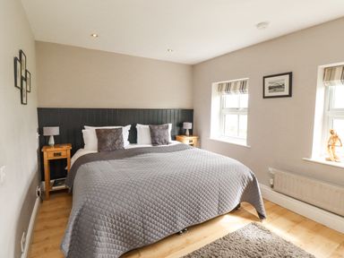 A bedroom with a large bed bedside tables and two windows at Adderstone Cottage in Bamburgh