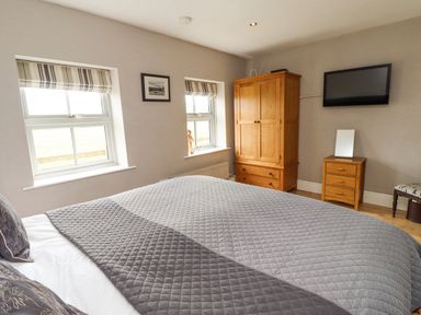 A bedroom with a bed a wooden wardrobe a wooden bedside table with a mirror and a wall-mounted television at Adderstone Cottage in Bamburgh