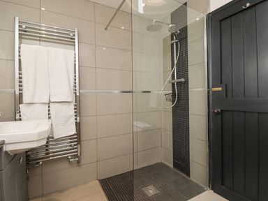 A bathroom with a walk-in shower a towel rack with towels a sink and a black door at Adderstone Cottage in Bamburgh